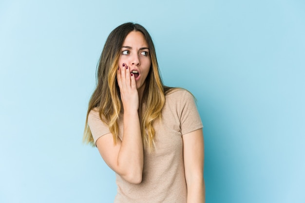 Jonge vrouw die op blauwe muur wordt geïsoleerd die wegens iets dat zij heeft gezien wordt geschokt