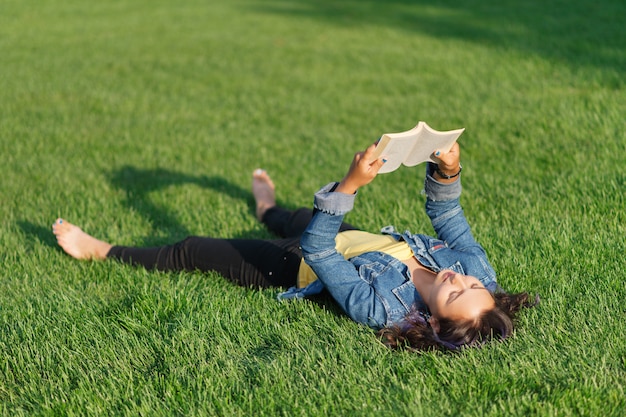 Jonge vrouw die op een groen gazon in het Park in de zomer ligt en een boek leest