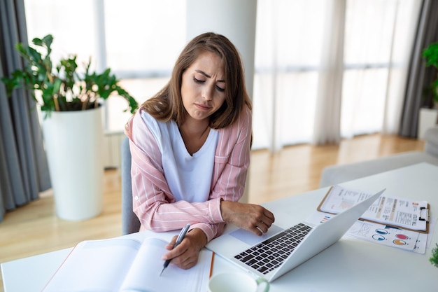 Jonge vrouw die op een laptop werkt Bedrijfsvrouw die bezig is met het werken op een laptop op kantoor Bedrijvsvrouw die op een helder modern werkstation zit en op een laptop schrijft