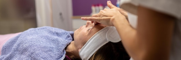 Jonge vrouw die op een massagetafel ligt en een gezichtsmassage krijgt