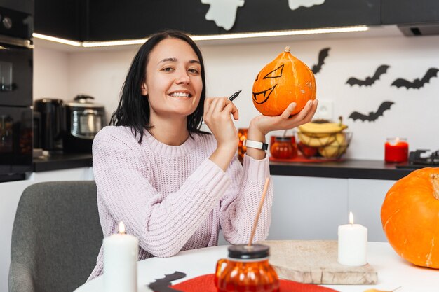 Jonge vrouw die op een pompoen trekt voor Halloween en naar de camera kijkt