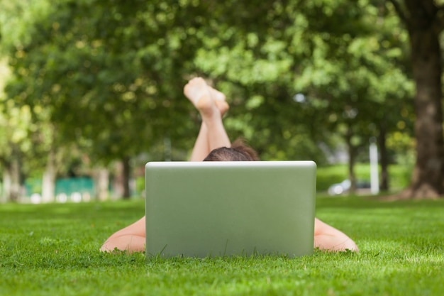 Jonge vrouw die op gras voor laptop ligt