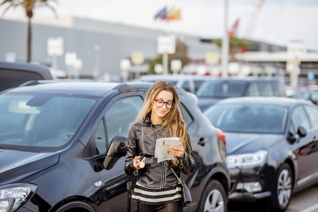 Jonge vrouw die op het huurcontract kijkt dat buiten op de parkeerplaats van de luchthaven staat