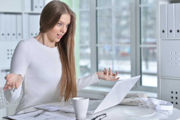 Jonge vrouw die op kantoor werkt met behulp van laptop