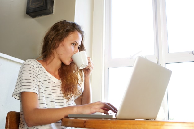 Jonge vrouw die op laptop werkt en koffie drinkt