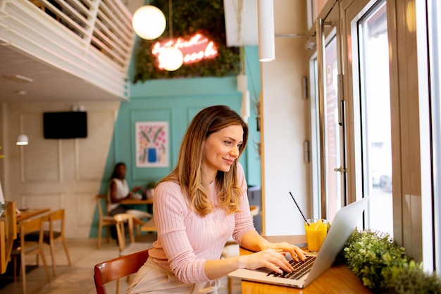 Jonge vrouw die op laptop werkt en verse jus d'orange drinkt in het café