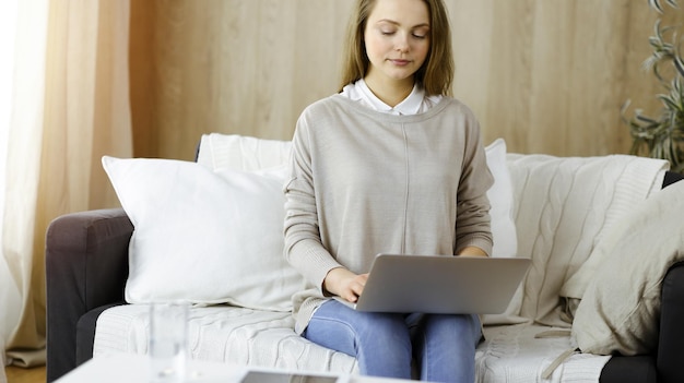 Jonge vrouw die op laptopcomputer werkt die binnenshuis zit tijdens Covid-19 quarantaine. Blijf thuis concept bij Coronavirus pandemie.