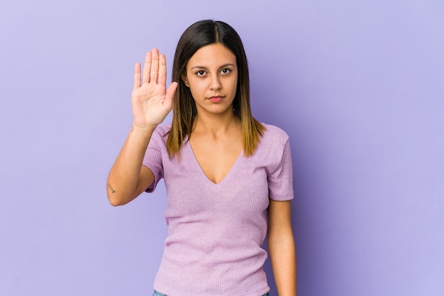 Jonge vrouw die op purpere status met uitgestrekte hand wordt geïsoleerd die stopbord toont, dat u verhindert.