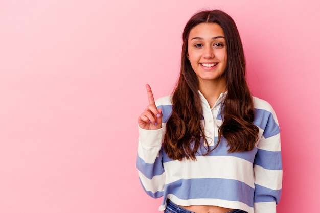 Jonge vrouw die op roze muur wordt geïsoleerd die nummer één met vinger toont