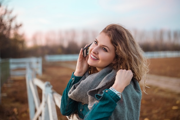 Jonge vrouw die op telefoon op de herfstgebied spreekt.