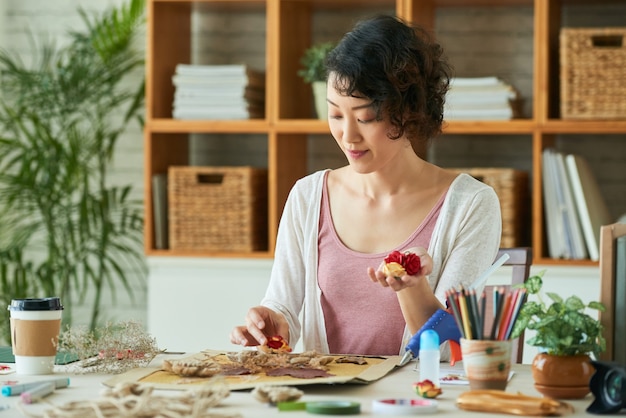 Jonge vrouw die oshibana-kunst beoefent, gebruikt geperste bloemen en andere botanische materialen om ...