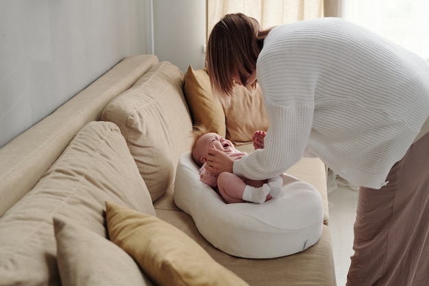 Jonge vrouw die over de bank buigt met haar schattige huilende babydochter