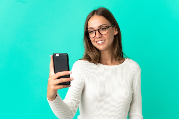 Jonge vrouw die over geïsoleerde blauwe achtergrond een selfie met mobiele telefoon maakt