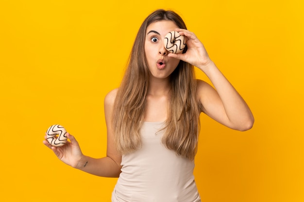 Jonge vrouw die over gele muur een doughnut in een oog houdt