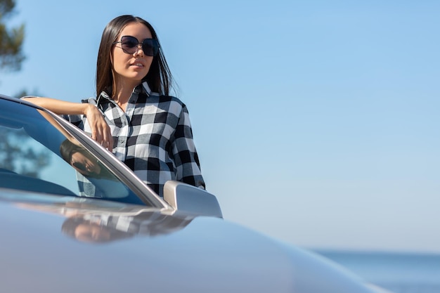 Jonge vrouw die overdag cabrio op de weg leunt