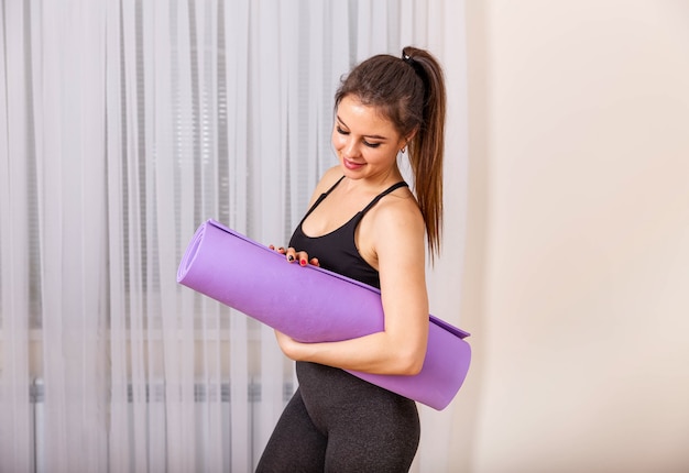 Jonge vrouw die paarse yoga- of fitnessmat vouwt na het sporten