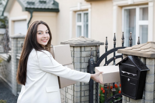 Jonge vrouw die pakketten naar huis draagt met een hoop kartonnen dozen Concept van online goederen kopen en thuis afleveren