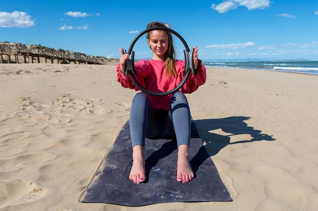 Jonge vrouw die pilateshoepel op het strand toont