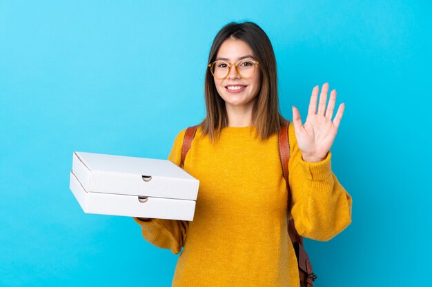 Jonge vrouw die pizzadozen over geïsoleerde blauwe muur houdt