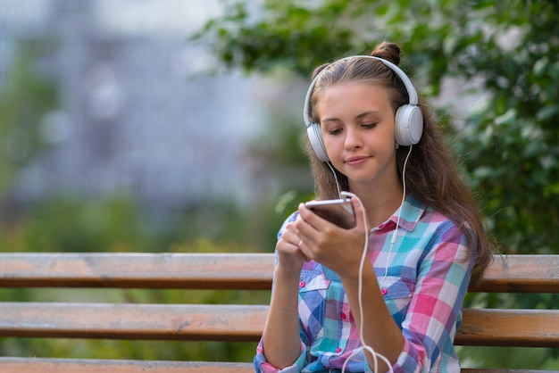 Jonge vrouw die probeert te beslissen over een nieuwe soundtrack die met een bedachtzame uitdrukking naar haar mobiele telefoon kijkt terwijl ze buiten naar muziek luistert