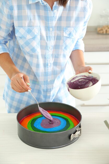 Jonge vrouw die regenboogcake in keuken maakt