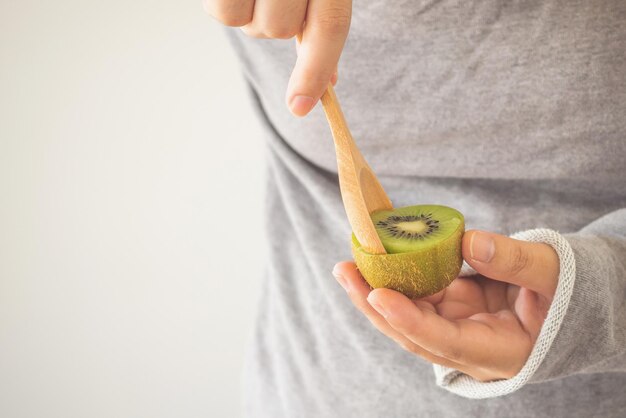 Jonge vrouw die rijpe kiwi's eet met houten lepel