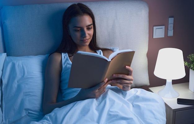 Jonge vrouw die 's nachts een boek in bed leest