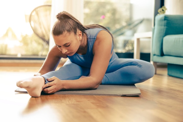 Jonge vrouw die 's ochtends thuis traint. Ze doet stretching training op oefenmat.