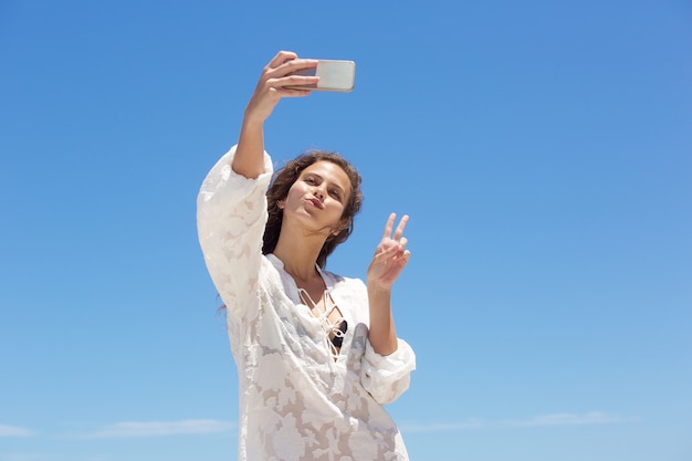 Jonge vrouw die selfie met het teken van de vredeshand nemen