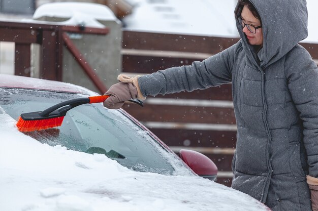 Jonge vrouw die sneeuw van auto borstelt na zware sneeuwval