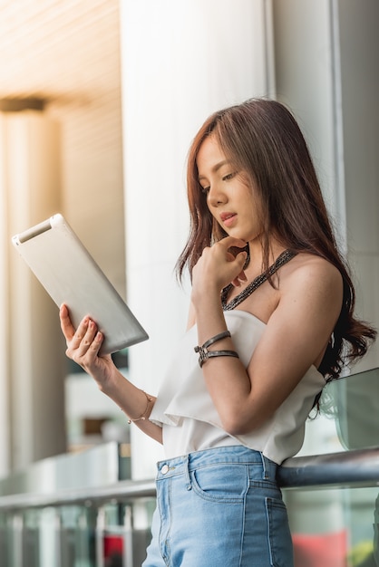 Jonge vrouw die tablet in de bouw van het glazenbureau gebruiken.