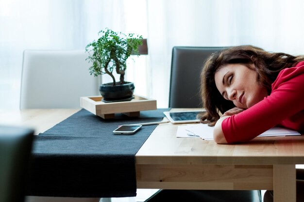 Jonge vrouw die telefoon gebruikt terwijl ze op tafel zit