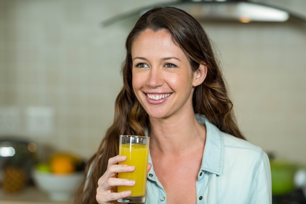 Jonge vrouw die terwijl het drinken van sap in keuken glimlacht