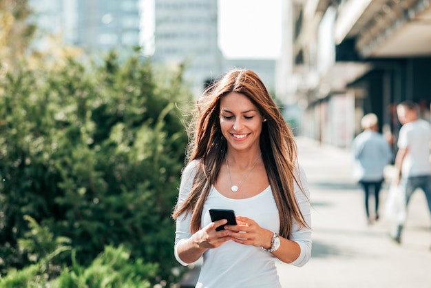 Jonge vrouw die terwijl het lopen in de stadsstraat texting.