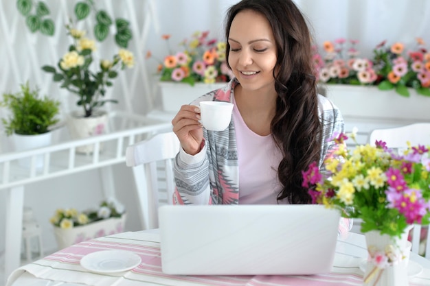 Jonge vrouw die thee drinkt en laptop gebruikt