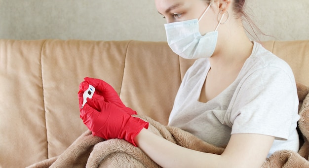 Foto jonge vrouw die thermometer kijkt en beschermend masker draagt, preventie van coronavirus