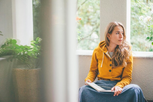 Jonge vrouw die thuis bij het raam zit