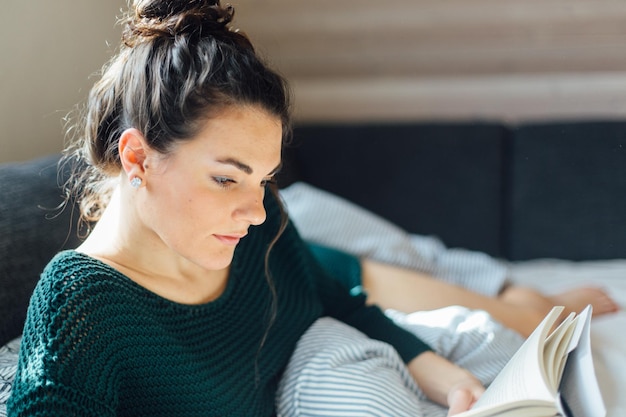 Jonge vrouw die thuis een boek leest terwijl ze op bed ligt