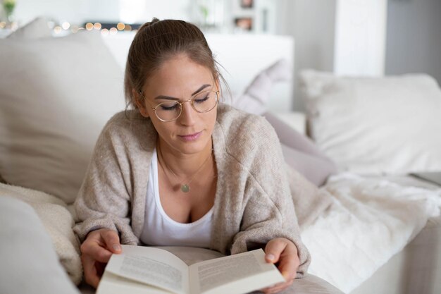 Foto jonge vrouw die thuis een boek leest terwijl ze op bed ligt