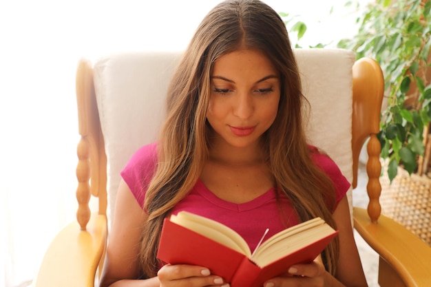 Foto jonge vrouw die thuis een boek leest