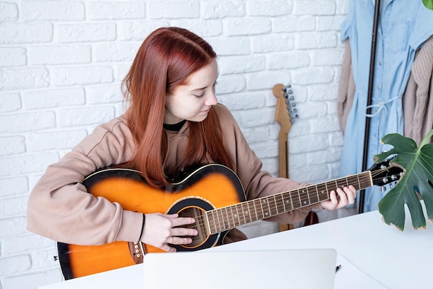 Jonge vrouw die thuis gitaar leert spelen