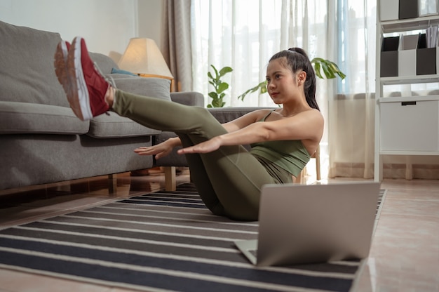 Jonge vrouw die thuis in een woonkamer traint Jonge vrouw die oefeningen online herhaalt workout