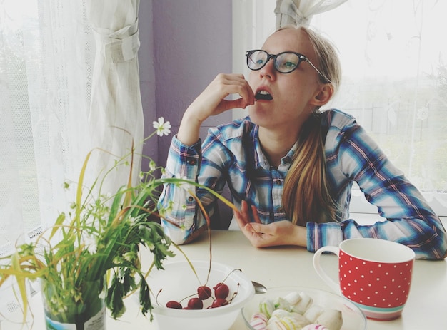 Foto jonge vrouw die thuis kersen eet