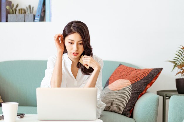 Jonge vrouw die thuis online winkelt met creditcard en laptop