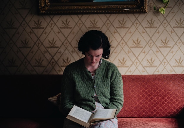 Jonge vrouw die thuis op de bank zit en een boek leest