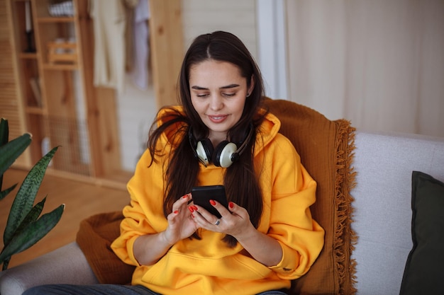 Jonge vrouw die thuis zit met een smartphone in haar handen en naar het scherm kijkt