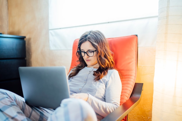 Jonge vrouw die van bed thuis met computer werkt.