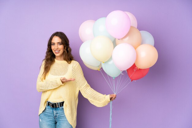 Jonge vrouw die veel ballons over op purpere muur vangt die handen aan de kant uitbreidt