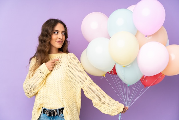 Jonge vrouw die vele ballons over op purpere muur vangt