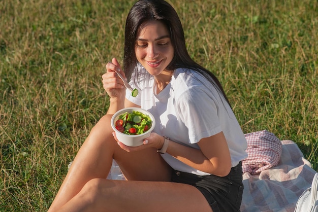 Jonge vrouw die verse salade eet in het park op het gras